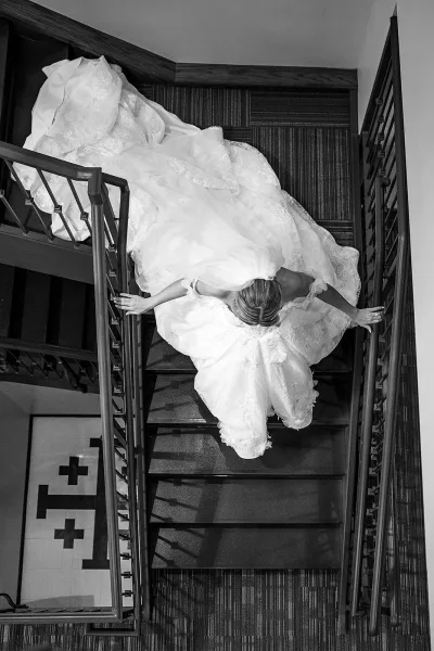 Bridal portrait of a bride descending a staircase, her gown’s long train cascading over the carpeted steps in an indoor setting.