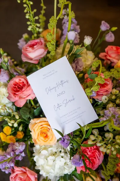 Wedding program with a ceremony program cover styled among roses, set against a dark backdrop for elegant contrast.