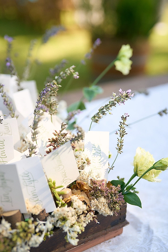 Wedding place cards with calligraphy place cards tucked into a wooden box with wildflowers and greenery on a lace tablecloth in a garden setting