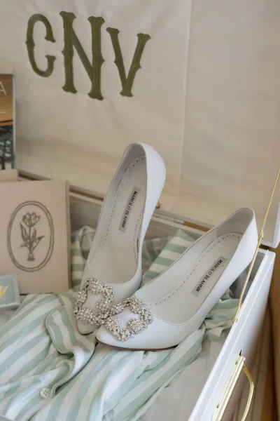 Wedding shoes, white high heels with a crystal buckle on a shoe box, styled on a tabletop with striped fabric and paper boxes
