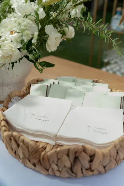 Wedding favor napkins and custom cocktail napkins wedding with handwritten calligraphy in a woven basket on a wood tabletop, mint cards nearby