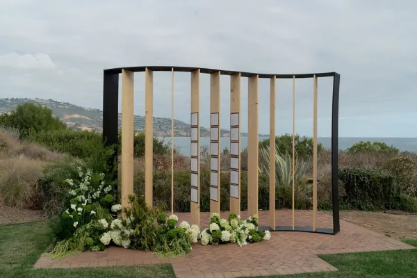 Modern wedding altar with geometric wedding arch, wood slat and black frame panels, white hydrangeas and calla lilies overlooking ocean hills