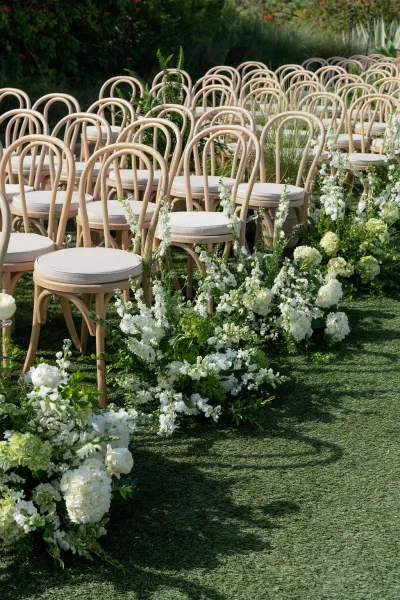 Ceremony seating with outdoor wedding ceremony seating in wood chairs and cushions, aisle lined with white flowers and greenery on lawn grass