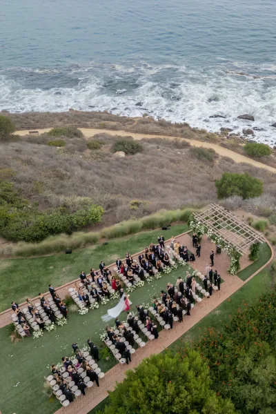 Outdoor ceremony setup with an oceanfront wedding ceremony arch and white florals, chairs and petal-lined aisle on a coastal bluff above waves