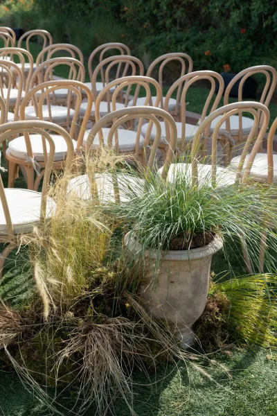 Ceremony seating with outdoor ceremony chairs in neat rows, wood chairs with white cushions beside a planter on a garden lawn
