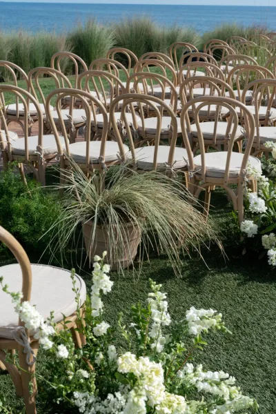 Ceremony seating with outdoor ceremony seating rows of wood chairs and cushions, flanked by floral ground arrangements by the ocean lawn