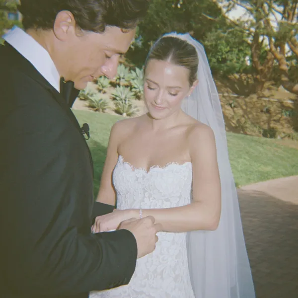 Wedding vows as bride in strapless lace dress and veil holds groom’s hands during couple exchanging vows on a sunlit garden walkway