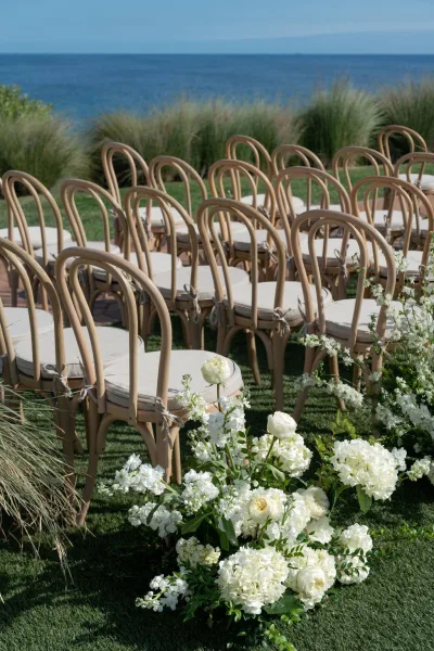 Ceremony seating with outdoor wedding ceremony chairs, wood bistro rows on a lawn aisle lined with white flowers and ocean view beyond