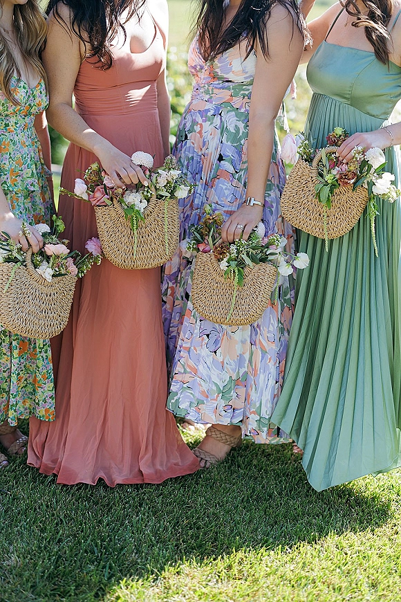 Bridesmaid bouquets held by bridesmaids holding bouquets, with woven straw handbags and pastel dresses on a sunlit grass lawn