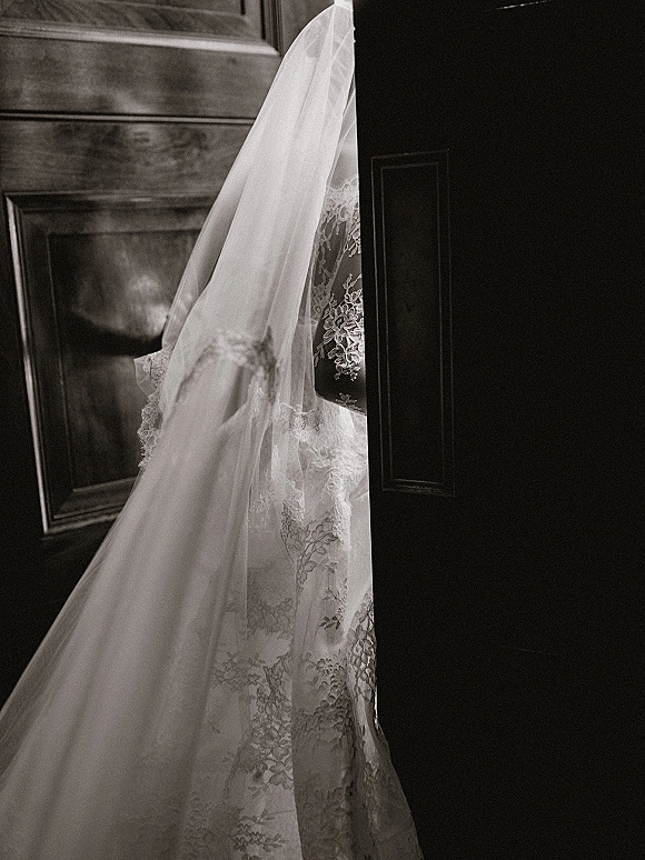 Bridal veil cascading into a cathedral veil over a lace wedding dress, sheer tulle trailing as she stands in a wooden doorway