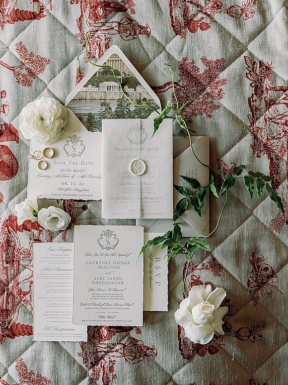 Invitation suite wedding stationery flat lay with wax seal, RSVP and save the date cards, rings, and white florals on toile fabric