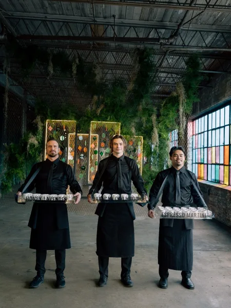 Wedding cocktail service with signature cocktail display of espresso martini shots on trays, set against a greenery wall in an industrial warehouse venue