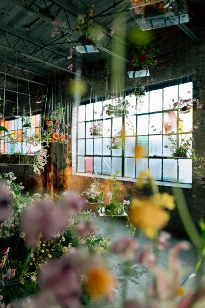 Hanging floral installation of suspended wedding flowers on acrylic shelves with wildflower accents in an industrial loft with brick walls