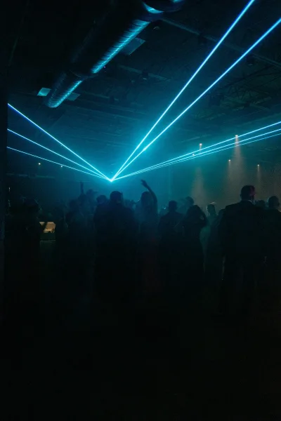 Wedding dance floor packed with guests at a reception dance party, blue laser lights and haze cutting through an industrial ceiling and ducts