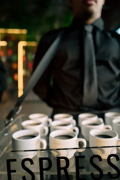 Espresso bar wedding coffee bar with an espresso machine and white coffee cups, set under warm bistro lighting in a blurred interior setting