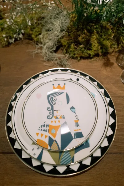 Wedding place setting with gold rim plates and patterned black-and-white dishes, greenery centerpiece and glasses on a rustic wood table