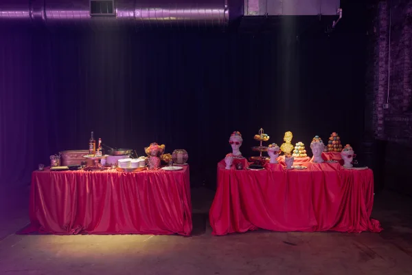 Dessert table display with macaron towers, cupcakes and pastries on red linens, chalkboard menu signs, purple uplighting and brick wall backdrop