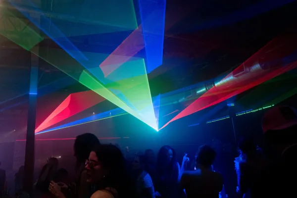 Wedding dance floor with wedding laser lights cutting through fog haze as crowd silhouettes move under colorful uplighting in an indoor venue