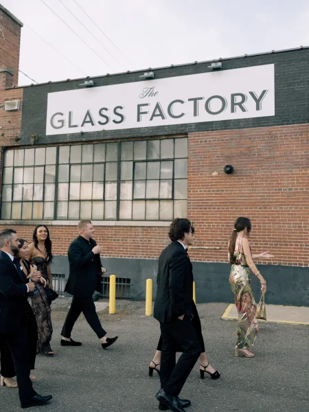 Wedding guests walking together in formalwear, wedding guests arrival outside a brick industrial venue, heels and jewelry under an overcast sky