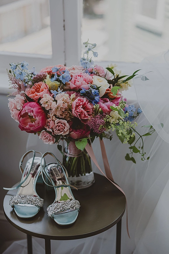 Bridal bouquet with pink peonies and roses, blue delphinium and greenery, tied with pink ribbon on a side table by window light