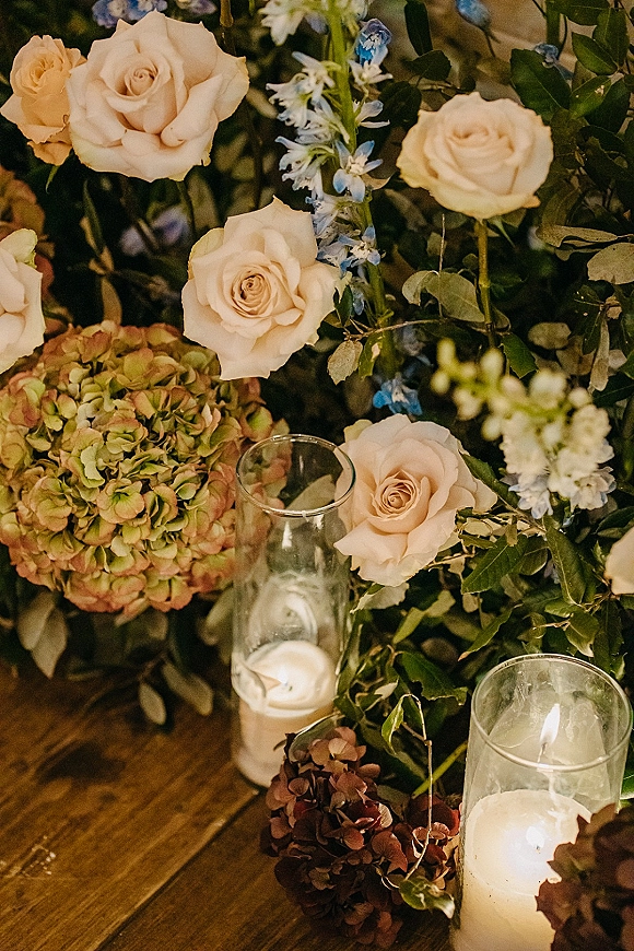 Wedding floral centerpiece with cream roses and hydrangea, plus pillar candles in glass hurricane vases on a rustic wood table