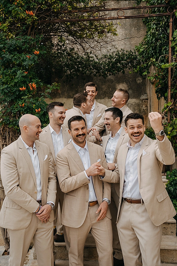Groomsmen portrait of the groom and groomsmen photo laughing in tan suits on stone steps with ivy vines and a pergola arch behind