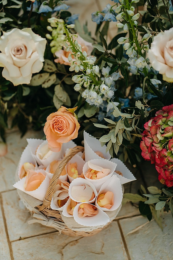 Flower girl basket with rose petal basket cones filled with petals, set on a stone patio beside lush floral arrangements