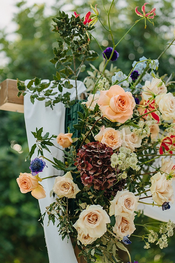 Wedding ceremony flowers on a chair with peach roses, hydrangea and greenery, framed by draped white fabric in a garden setting