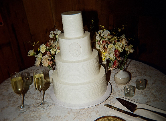 Wedding cake three tier wedding cake with monogram topper, flowers, champagne flutes, and candles on a lace-covered table against wood paneling