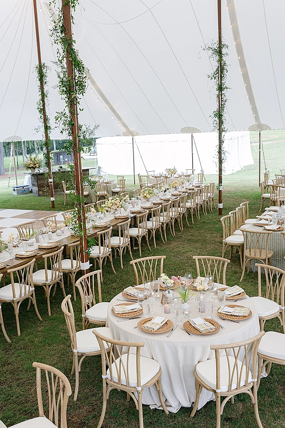 Wedding reception tent with sailcloth canopy, long banquet tables and candles, greenery garlands and string lights on a lawn