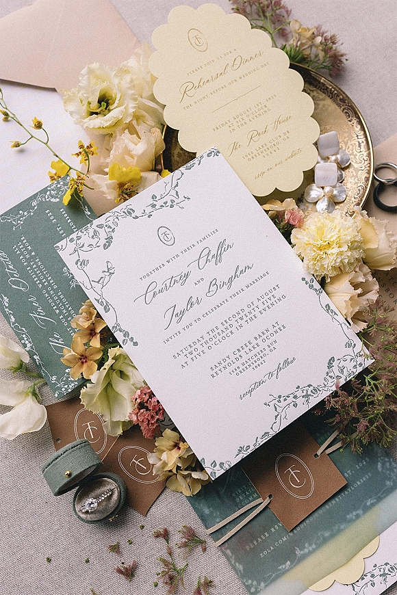 Wedding invitation suite flat lay with floral border cards, wax seal, ribbon, velvet ring box and scissors on linen fabric backdrop