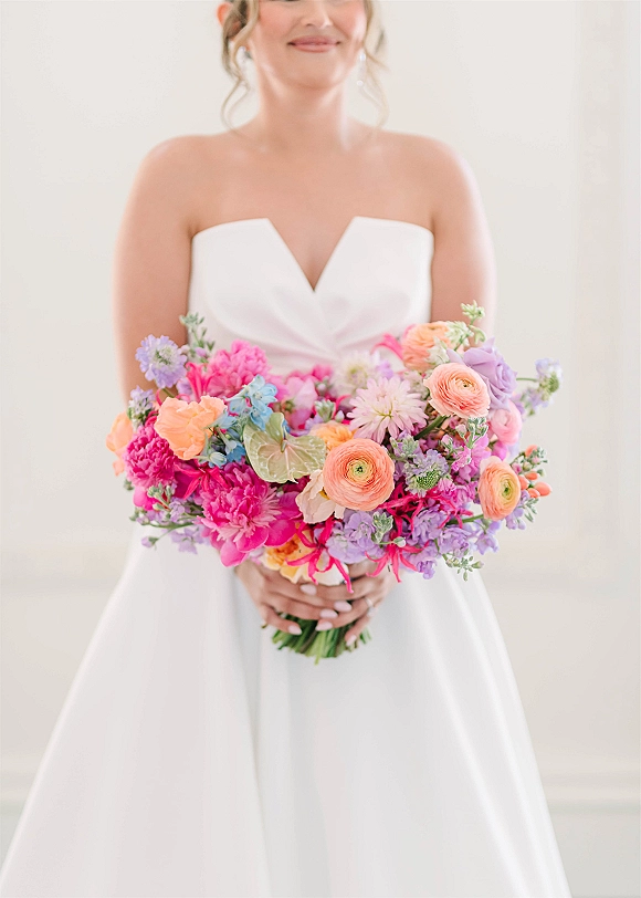 Bridal bouquet in a bride’s hands, a bright wedding bouquet of ranunculus, peonies and anthurium against a light neutral wall