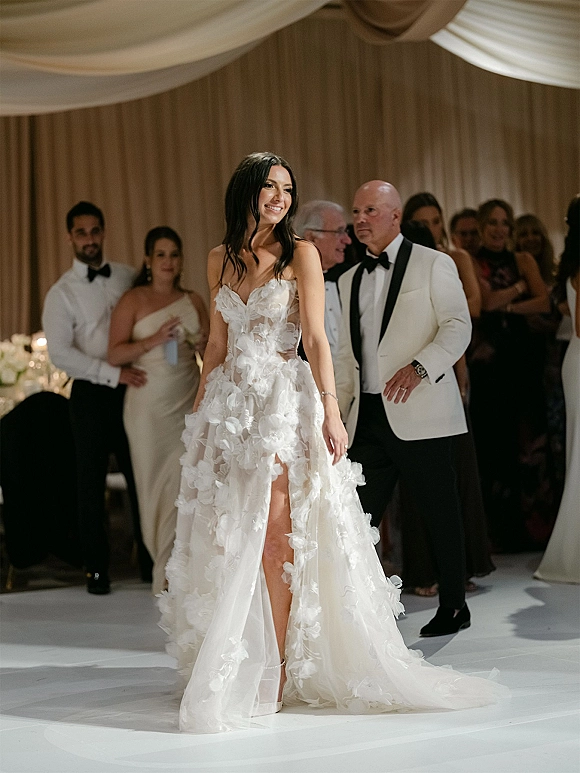 Bride entrance with groom in a white dinner jacket, she in a strapless floral appliqué gown, entering under draped ceiling to guests on dance floor