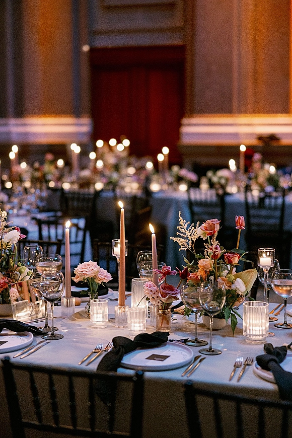 Reception tablescape with candlelit wedding reception taper candles, ribbed glass votives, floral centerpieces, and gold flatware in a dim hall