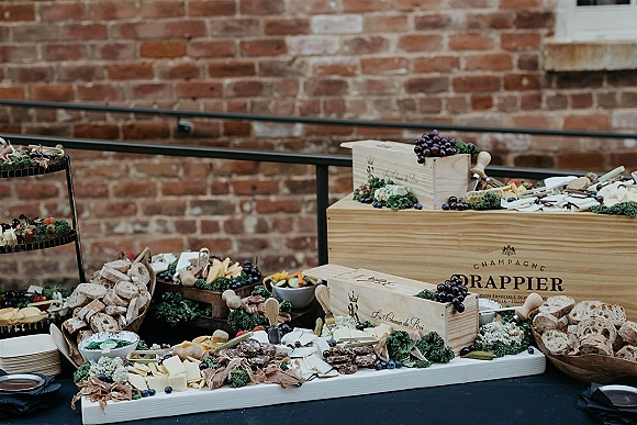 Charcuterie table with cheese assortment, cured meats, bread, grapes and berries on wooden trays, set against a brick wall background
