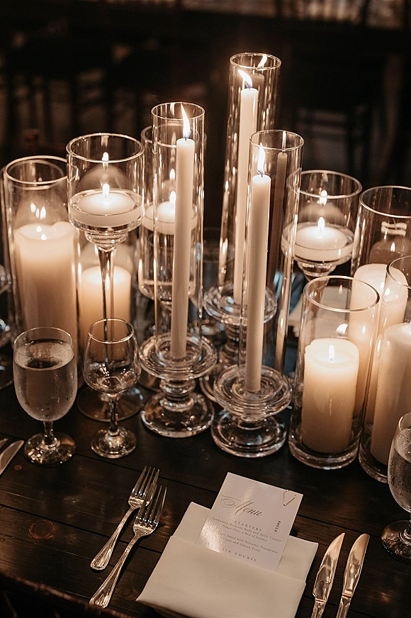 Reception tablescape with candlelit reception table featuring white taper and floating candles in glass cylinders on a dark wood table