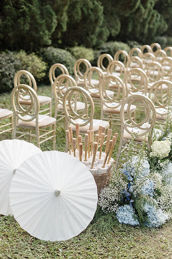 Ceremony seating with outdoor ceremony chairs in neat rows, white paper parasols and fan basket by hydrangea aisle florals on a lawn