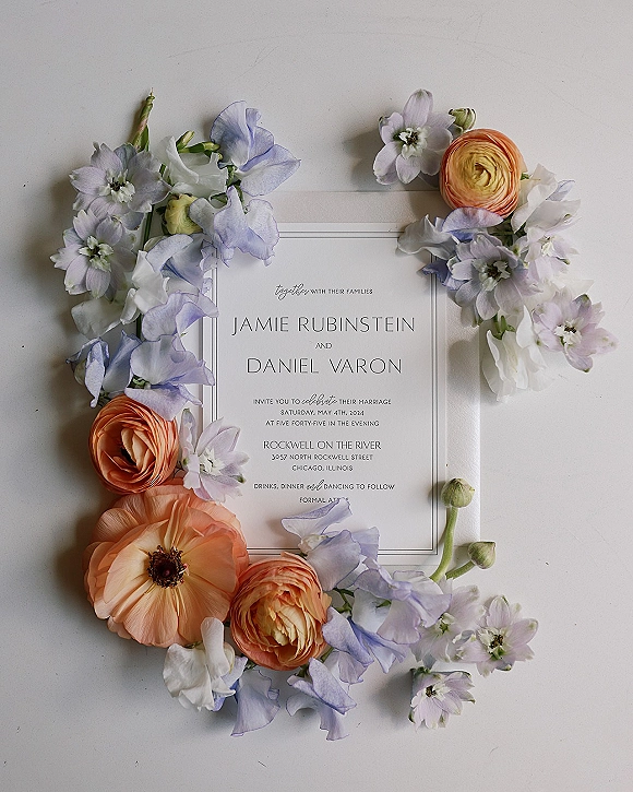 Wedding invitation flat lay with pastel ranunculus and sweet pea floral styling on a clean white surface, featuring crisp printed typography