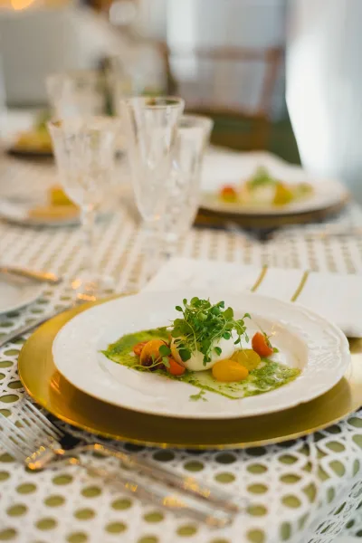 Reception tablescape with a wedding place setting featuring a gold charger plate, crystal glassware, and lace table runner among place cards