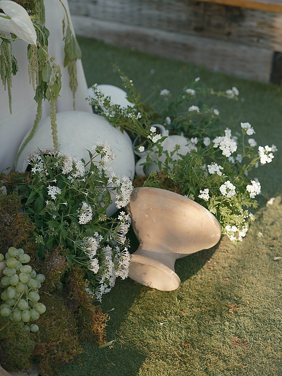 Ceremony aisle decor with wedding aisle floral ground arrangements, white pumpkins and moss clusters on grass before a wood wall backdrop