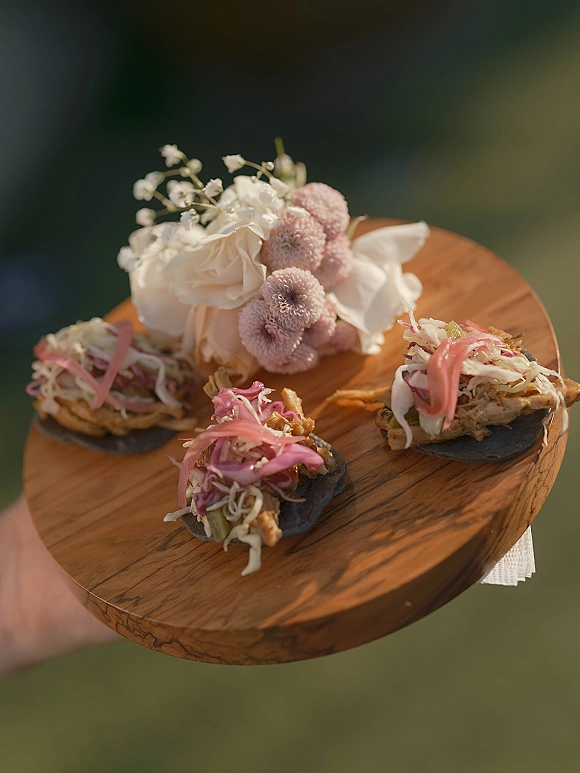 Wedding cocktail appetizers on a wood serving board, passed hors d'oeuvres of mini tostadas with pickled onions and slaw outdoors