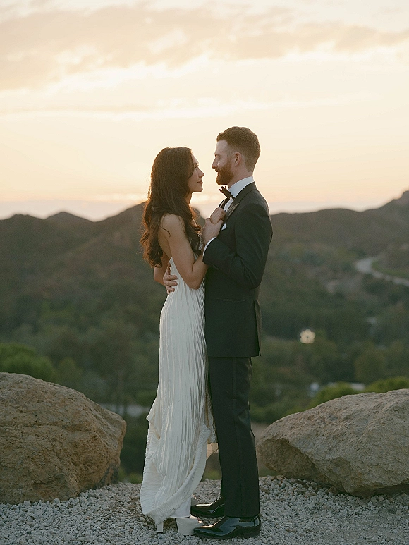 Couple portrait at sunset, sunset wedding portraits of bride in a long wedding dress and groom in tuxedo embracing by mountain boulders