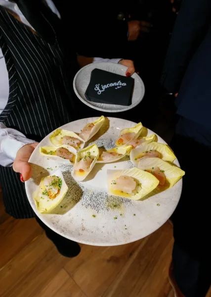 Wedding passed appetizers arranged as cocktail hour canapes in endive leaves on a ceramic plate, held by a server among guests on wood floor
