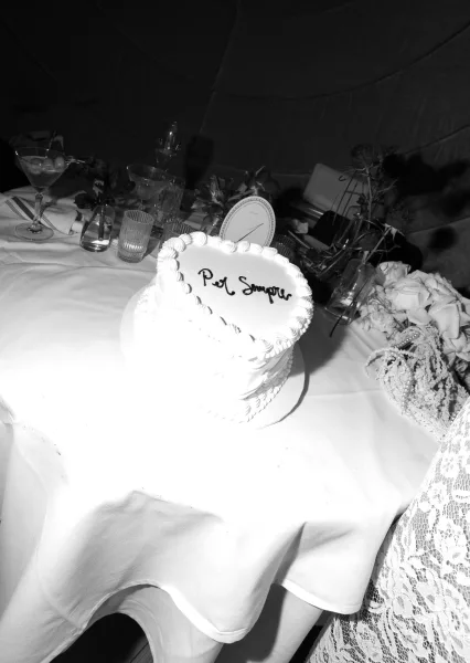 Wedding cake with heart shaped wedding cake design, white piped frosting on a stand beside champagne coupes, menu card, bud vases on tablecloth