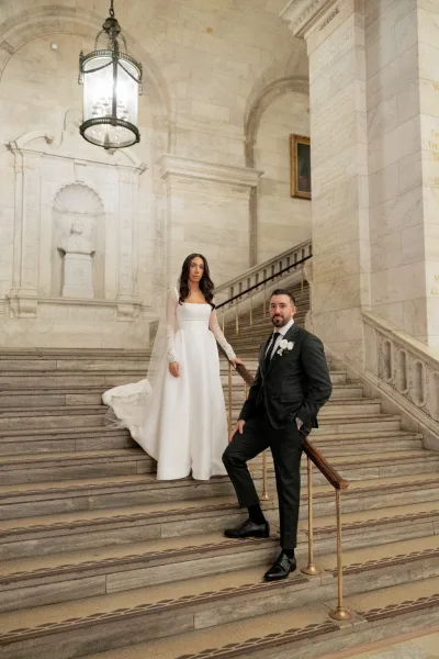 Couple portrait of bride and groom on stairs, her long-sleeve gown and veil train draped along a grand stone staircase with lanterns