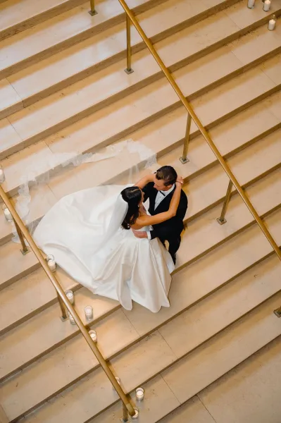 Couple portrait of bride and groom embrace on an indoor stone staircase, overhead view highlighting her veil and bridal train with candles