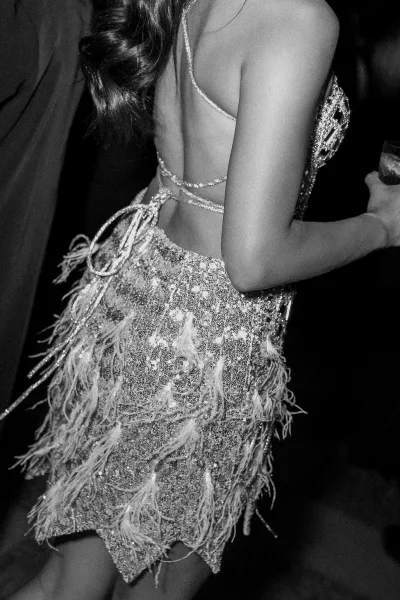 Wedding reception dress with a backless beaded lace-up design and feather fringe, worn under dim reception lighting with guests in the background