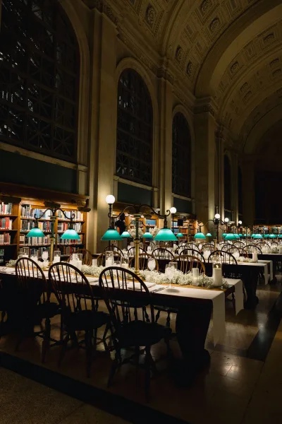 Reception tablescape with long banquet tables, white linens, candles, baby’s breath garland and green banker lamps in a grand library hall