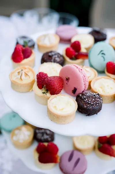 Wedding dessert table with macaron dessert bar featuring assorted macarons, mini fruit tarts, and berries on a white cake stand on linen