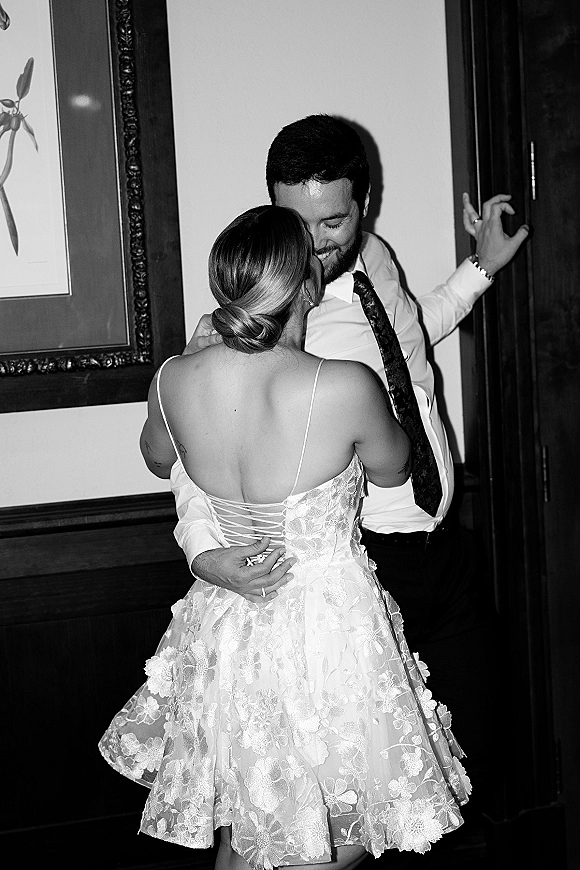 First dance moment in a black and white wedding photo, bride in lace corset-back dress and groom embracing near a wood-paneled wall